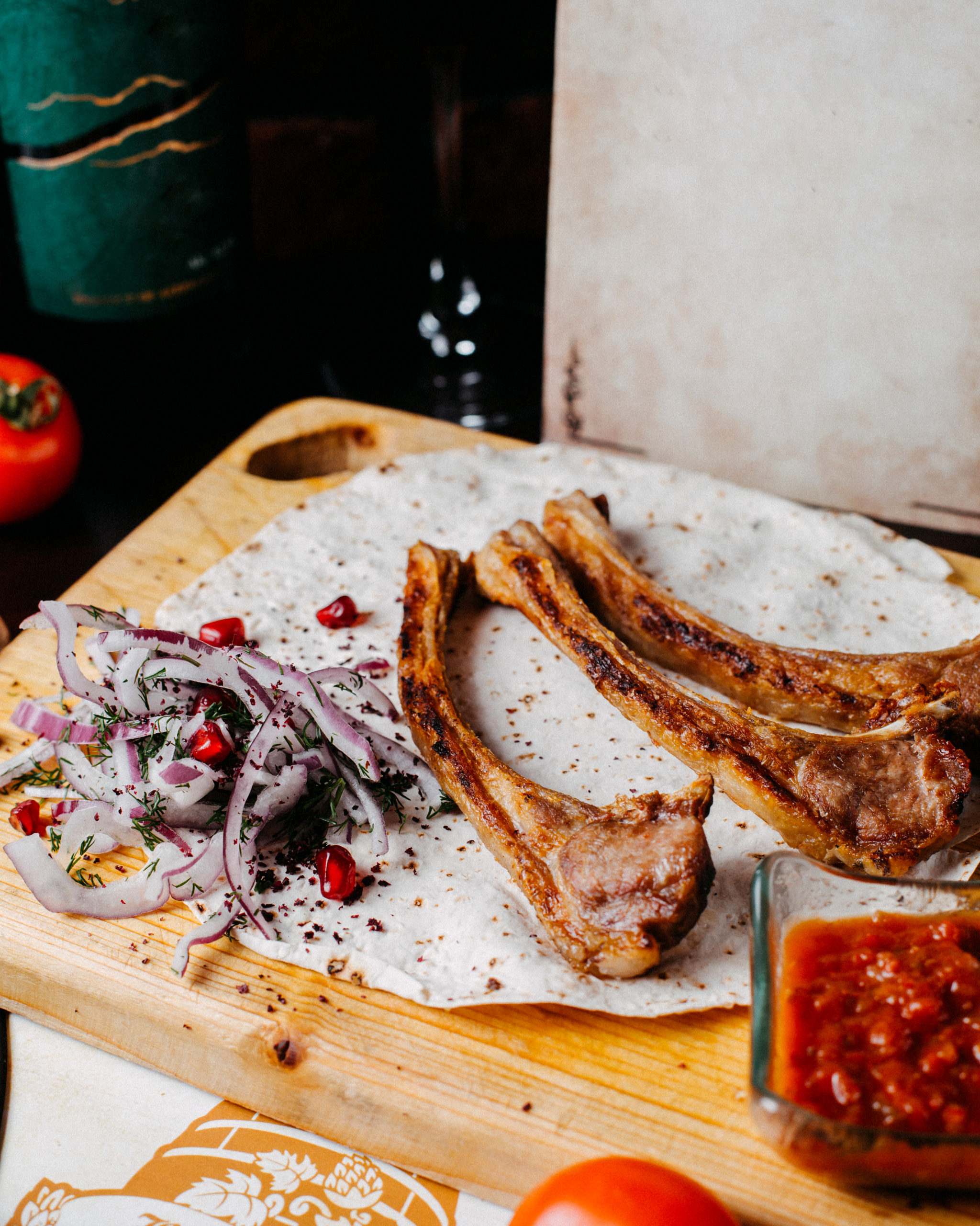 side view of kebab lamb ribs with red onion and pomegranate on a wooden board Lamb ribs with pomegranate.